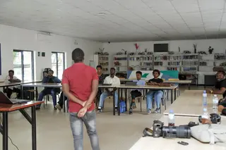 Instructor addressing a group of young adults in a classroom with camera gear