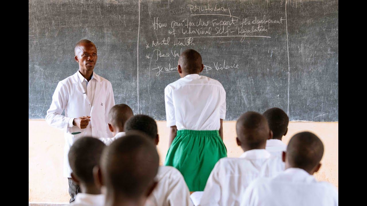 Teacher in a white coat leading a mental health and behavioral self-regulation workshop for students in a classroom.
