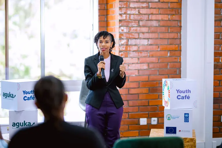 Woman speaking into a microphone at an Aguka Youth Café event presented by UNDP and the European Union.
